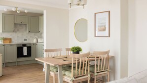 Una cocina moderna con armarios verde claro, una mesa de comedor de madera con sillas, una encimera blanca y una lámpara colgante.