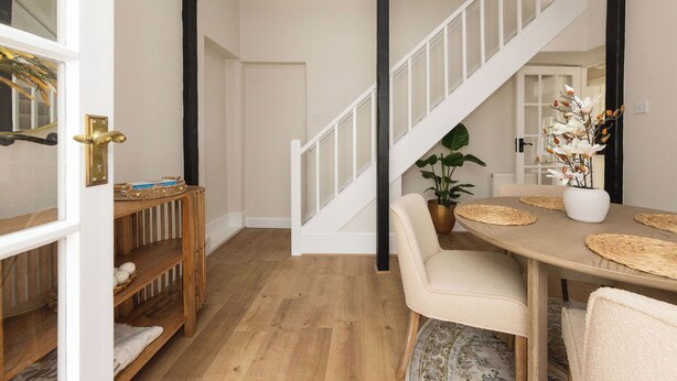 Ein Essbereich mit einem Holztisch, beigen Stühlen und einer Treppe mit weißen Geländern.