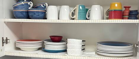 Una cocina con estantes que sostienen varias tazas y cuencos, una cafetera y un bloque de cuchillos.
