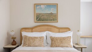 Una cama bien hecha con dos almohadas, una mesita de noche con una lámpara y un cuadro en la pared.