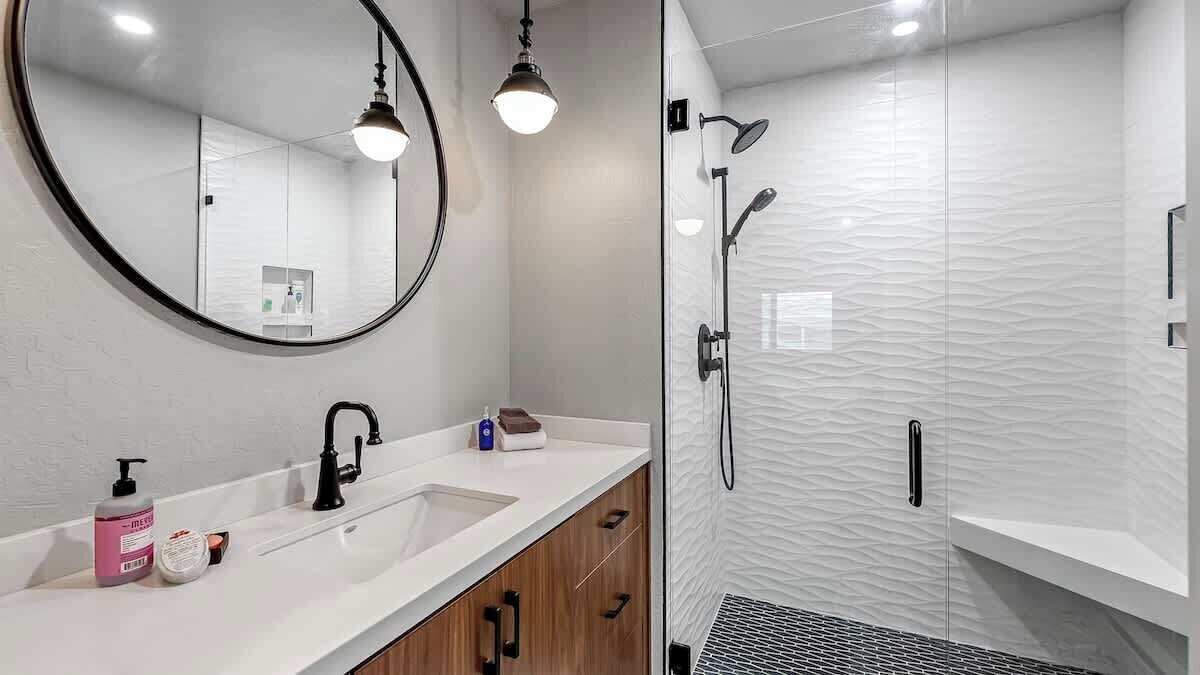 Een moderne badkamer met een wit wastafelmeubel, een ronde spiegel en een douche met een structuurwand.