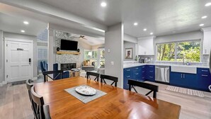 A modern kitchen with blue cabinets, a dining area with a wooden table, and a stone fireplace.