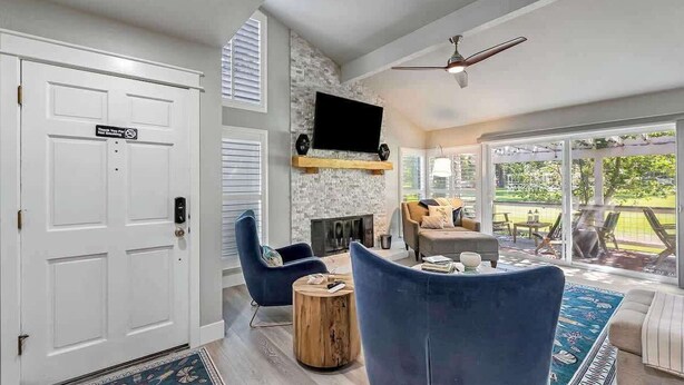 A living room with a fireplace, a television mounted on the wall, and a large window offering a view of the outdoors.