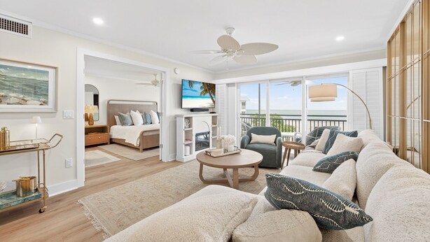 Ein geräumiges Wohnzimmer mit einer großen Couch, einem Couchtisch und einem Fernseher. Ein Balkon bietet Meerblick.