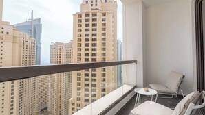 A balcony with a view of high-rise buildings, a small table, and a cushioned chair. - StayShort - JBR 2 Bed Apartment sleeps 4 with Sea Views! (Jumeirah Beach Residence)