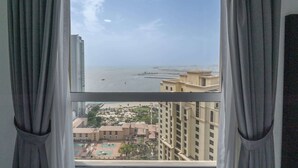 A view from a window with curtains, overlooking a coastal area with buildings and a beach. - StayShort - JBR 2 Bed Apartment sleeps 4 with Sea Views! (Jumeirah Beach Residence)