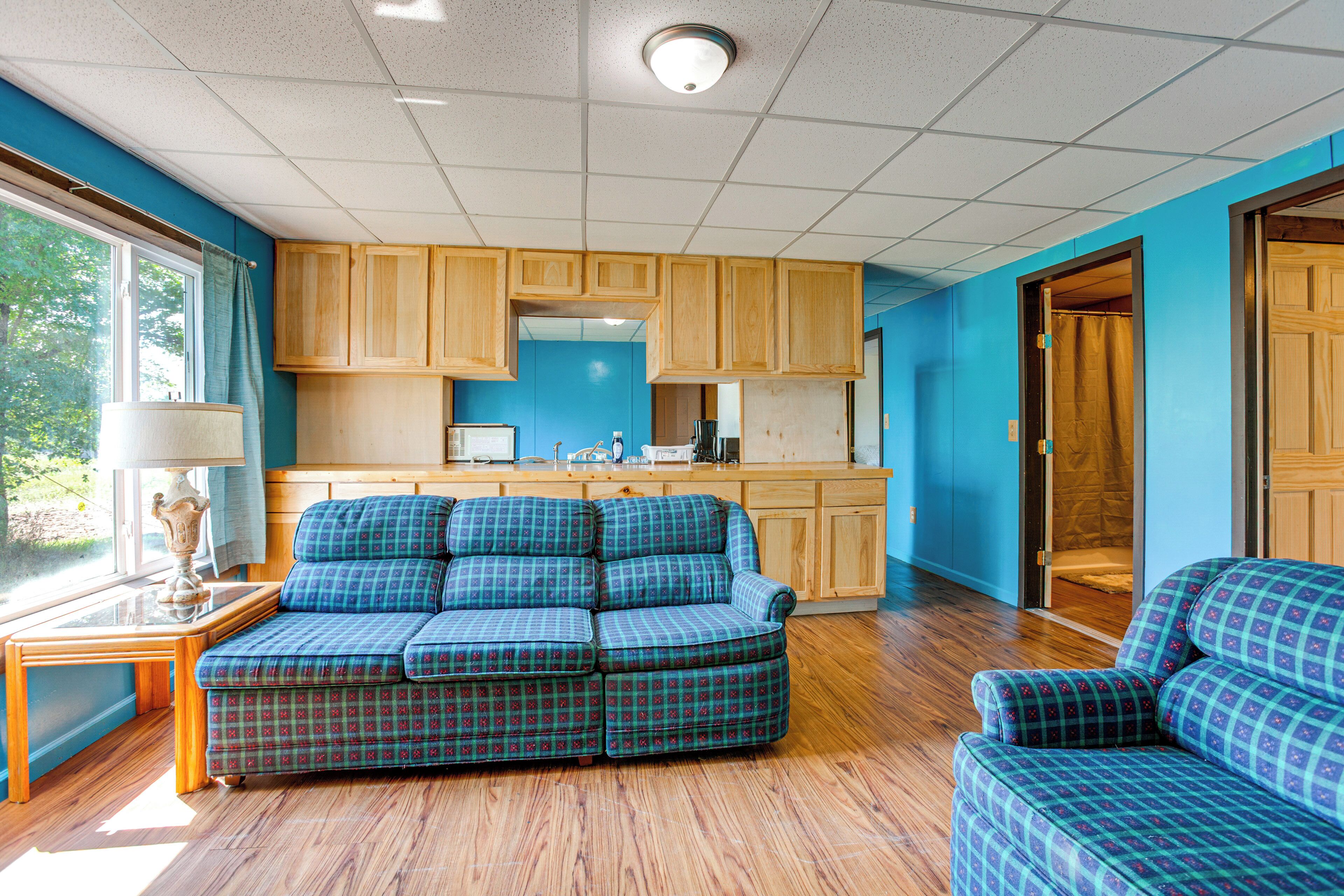 A room with a blue wall, wooden cabinets, a blue plaid sofa, and a wooden floor.