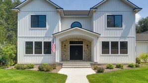 A two-story house with a central entrance, stone archway, and a flag on the left. - Ski & Hike in Kelly Canyon: Rigby Group Getaway (Rigby)