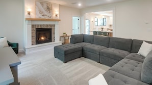 A modern living room with a sectional sofa, a fireplace, and a dining area in the background. - Ski & Hike in Kelly Canyon: Rigby Group Getaway (Rigby)