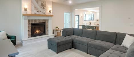 A modern living room with a sectional sofa, a fireplace, and a dining area in the background.