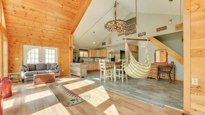A spacious living area with a large sofa, a dining table, and a hammock. - Fish + Hike: Wooded Home w/ Deck in Dexter (Dexter)