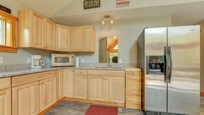 A modern kitchen with wooden cabinets, a stainless steel refrigerator, a microwave, and a coffee maker. - Fish + Hike: Wooded Home w/ Deck in Dexter (Dexter)