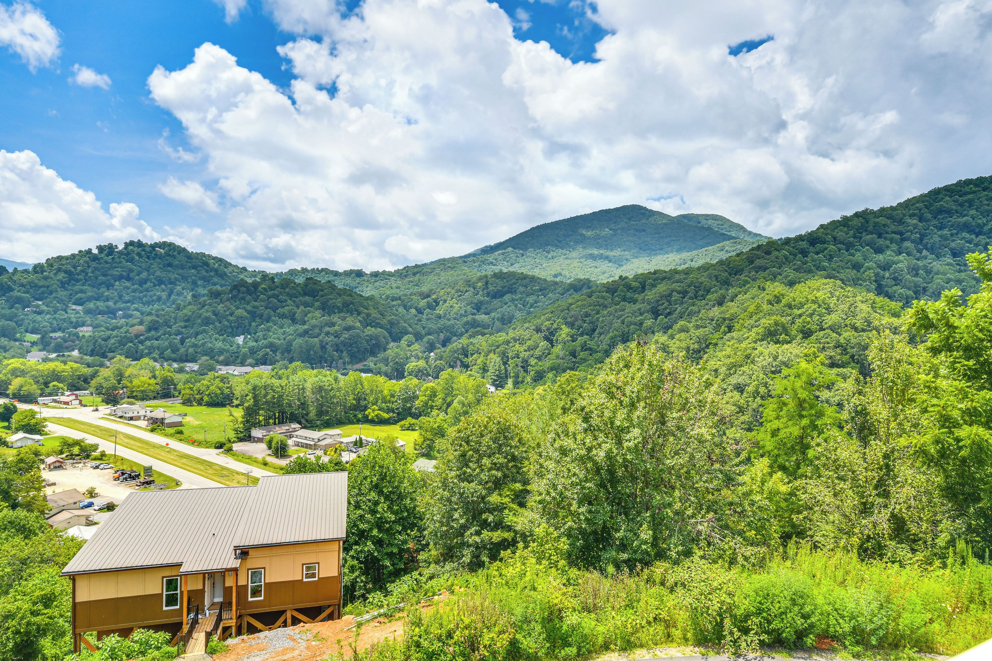 A house with a metal roof and a small porch, surrounded by lush green hills and a clear sky.