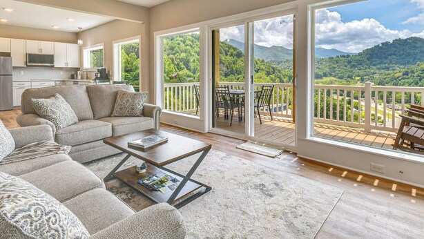 A spacious living area with a sofa, coffee table, and a view of a lush landscape through large sliding glass doors. - Smoky Mtn Getaway: Modern 2br/2ba W/stunning Views (Maggie Valley)