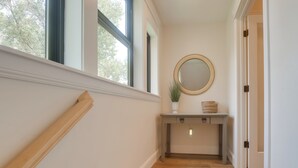 A hallway with wooden flooring, a white wall, a round mirror, and a small table with a plant and a basket. - Ski, Hike, Explore: Modern Guest Suite in Rigby (Rigby)