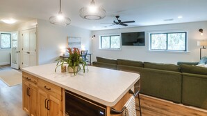 A modern kitchen with wooden cabinets, a central island, pendant lighting, and a green sofa in the living area. - Ski, Hike, Explore: Modern Guest Suite in Rigby (Rigby)
