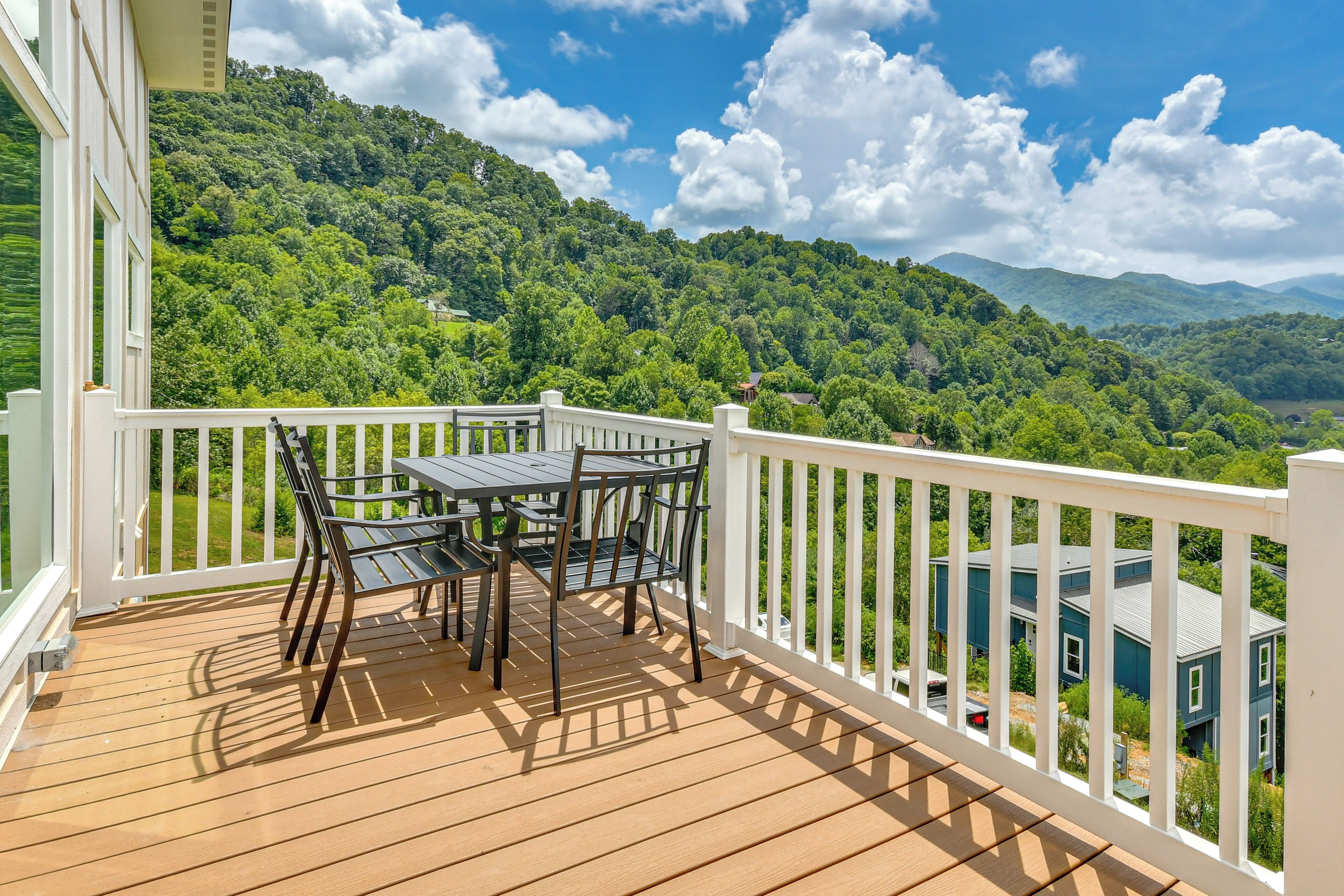 A wooden deck with a table and chairs, overlooking a lush green landscape and hills.