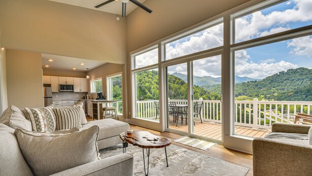 A spacious living room with a large window offering a mountain view, a cozy seating area with a coffee table, and a kitchen in the background. - Cozy 2br/2ba Mtn Escape w/ Views in Maggie Valley (Maggie Valley)