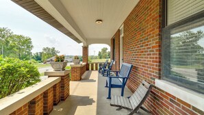 A covered patio with brick walls, a concrete floor, and a row of blue chairs and a wooden bench. - Remodeled Columbia Home: 14 Mi to St Louis (Columbia)