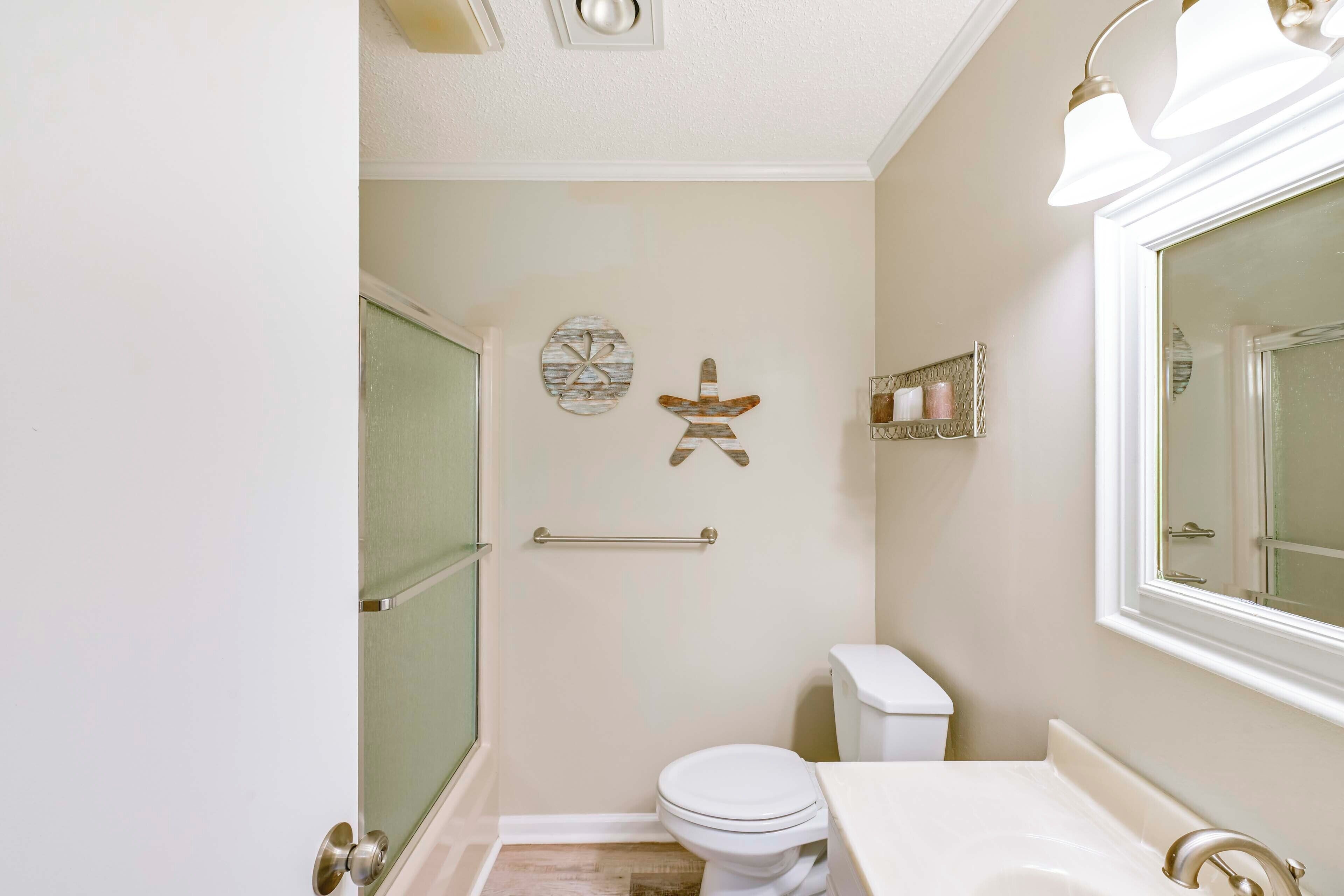 A bathroom with a toilet, sink, and shower. There are decorative wall hangings and a towel rack.