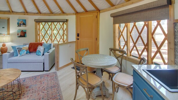 A cozy interior with a wooden ceiling, a dining area with a round table and chairs, a sofa with cushions, and a kitchen area with a sink. - Unplugged Retreat! Unique Yurt w/ Deck in Smokies (Sparta)