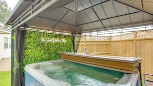A hot tub under a covered patio with a wooden fence and greenery in the background. - Hot Tub & Private Backyard! Gulfport Group Getaway (Gulfport)