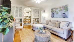 A living room with a sofa, a coffee table, and a ceiling fan. There are two paintings on the wall and a plant in the corner. - Hot Tub & Private Backyard! Gulfport Group Getaway (Gulfport)