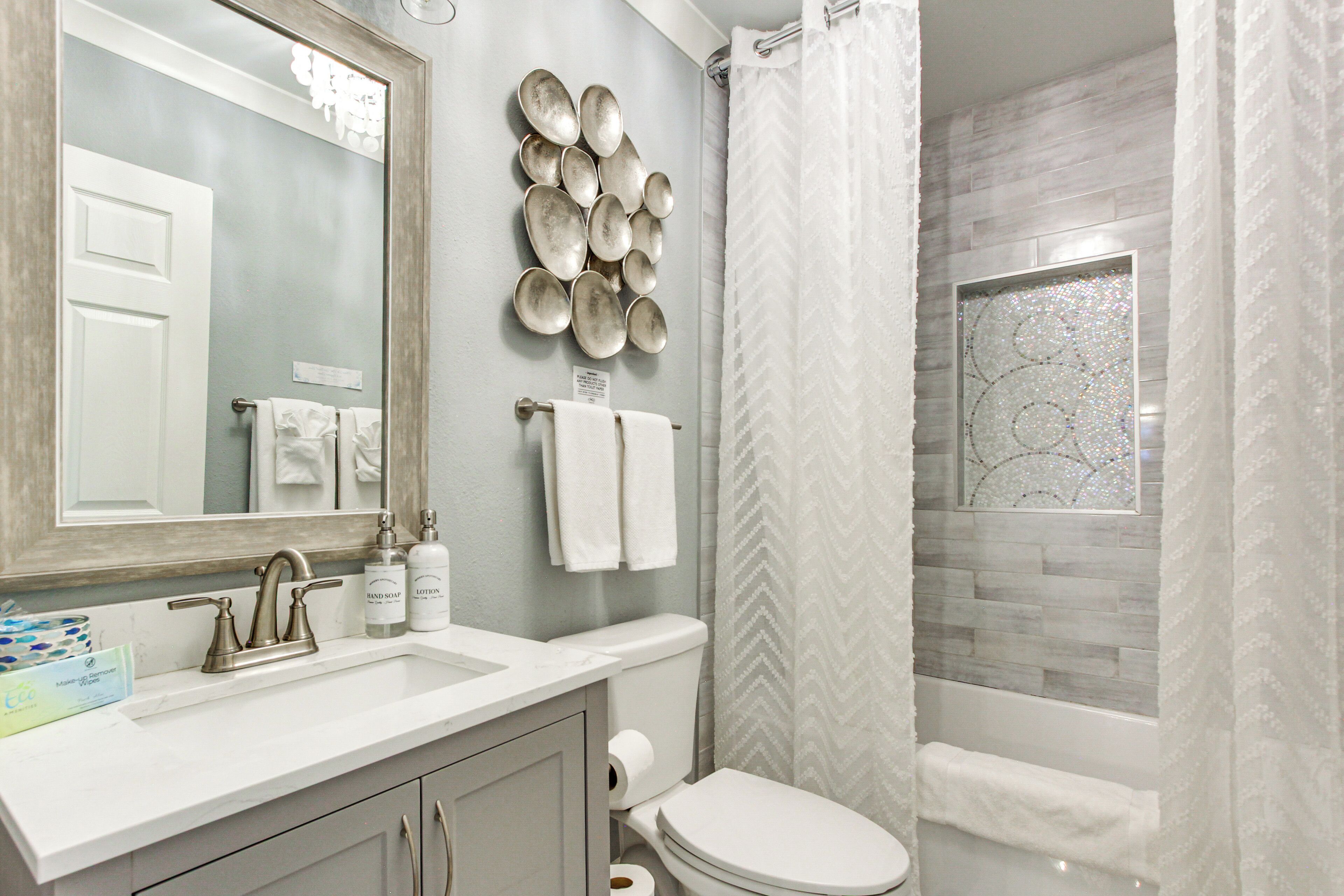 A bathroom with a white sink, mirror, and toilet, a shower curtain, and a decorative wall with plates.