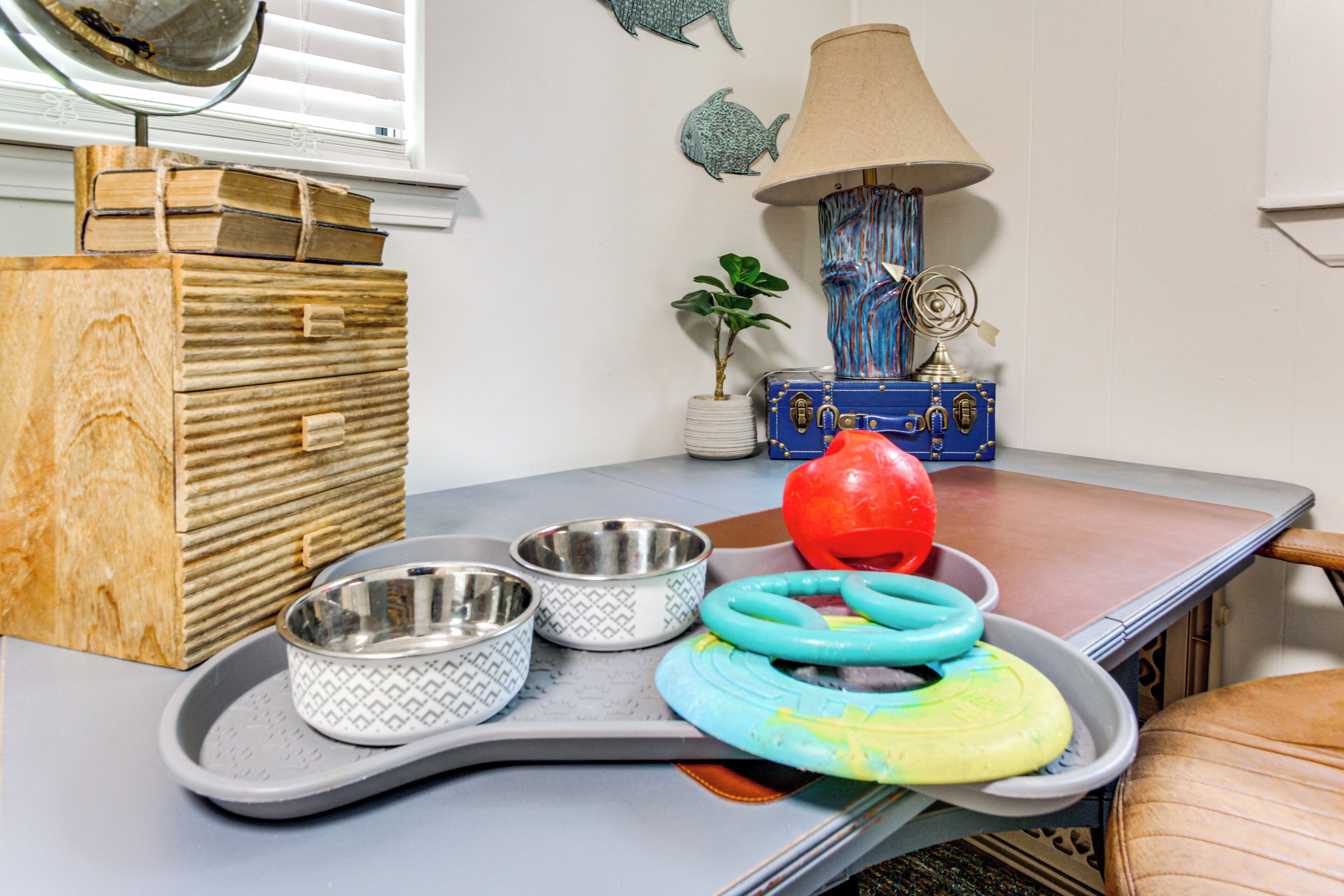 A room with a wooden chest of drawers, a lamp, a globe, and pet bowls on a tray.
