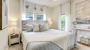 A bedroom with a bed, bedside lamps, a nightstand, a window with curtains, and a painting on the wall. - Hot Tub & Private Backyard! Gulfport Group Getaway (Gulfport)