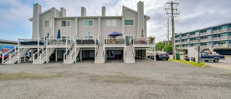 A two-story building with a central entrance, multiple balconies, and a gravel driveway.