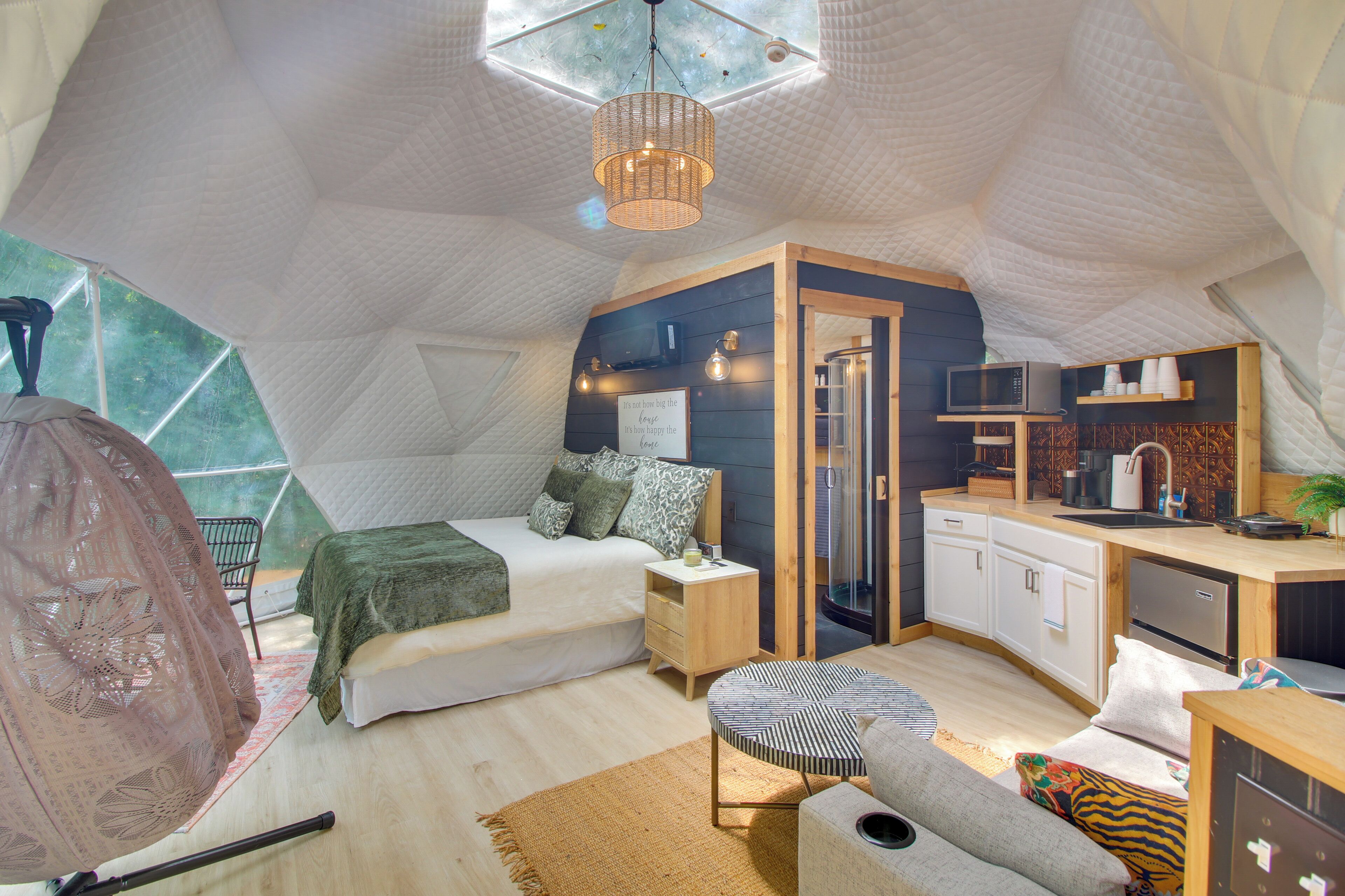 A cozy, triangular tent-style room with a bed, bedside table, and a kitchenette.