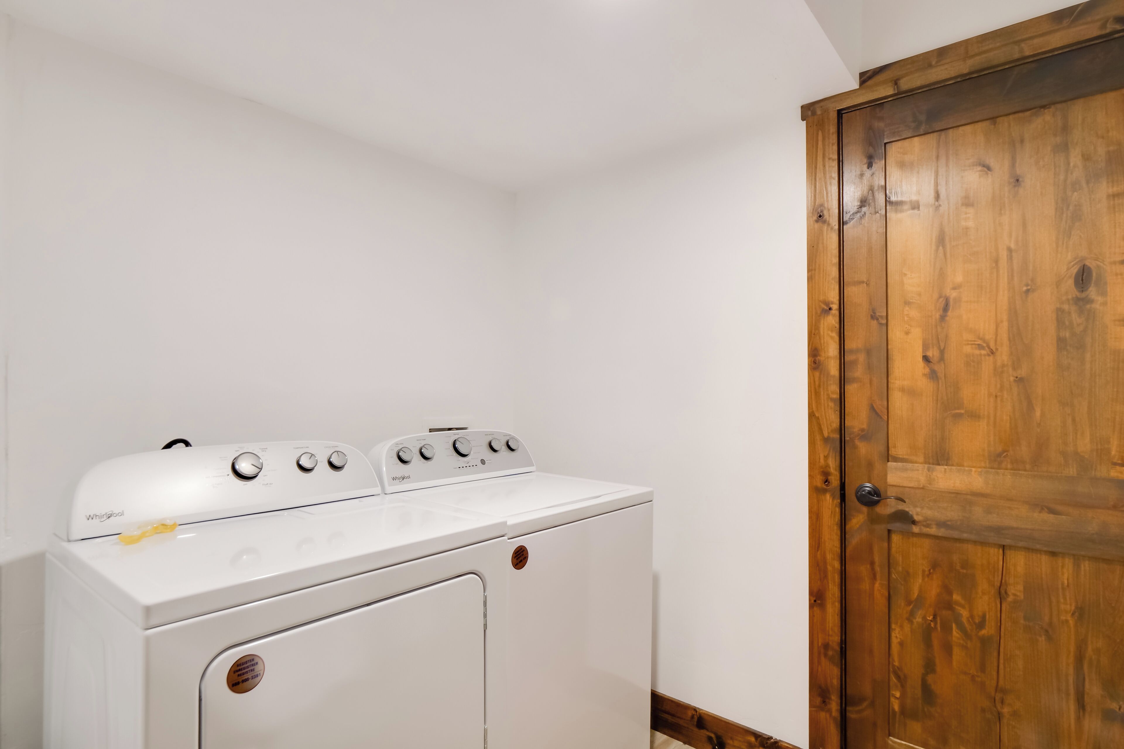 Un lavadero con lavadora y secadora Whirlpool blancas, una puerta de madera y paredes blancas.