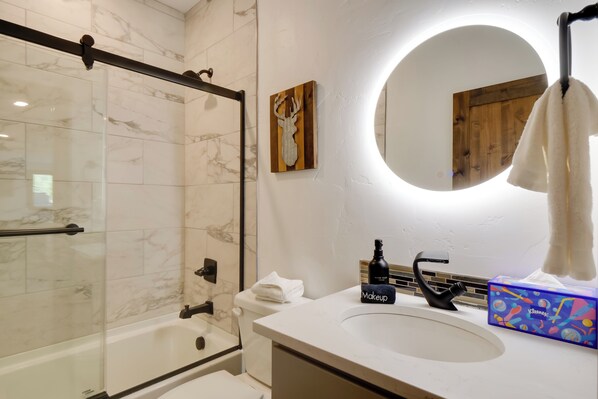Une salle de bain moderne avec une douche à parois de verre, un miroir rond et un lavabo blanc.