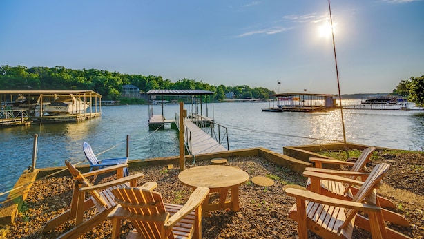 A lakeside dock with wooden chairs and tables, boats, and a covered area. - Dock & Prime Location: Lakefront Osage Beach Home (Osage Beach)