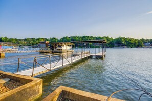 A dock with a covered boat and a small building, surrounded by calm water and greenery. - Dock & Prime Location: Lakefront Osage Beach Home (Osage Beach)