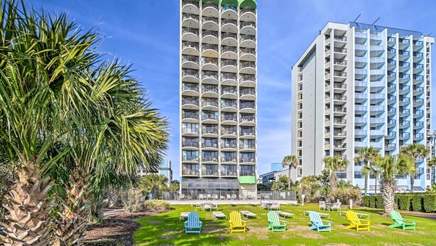 A tall hotel with multiple balconies and a well-maintained lawn with colorful chairs. - Prime Location + Ocean View: Myrtle Beach Condo! (Myrtle Beach)