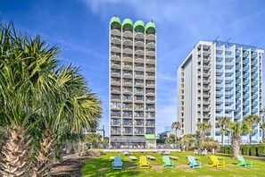 A tall hotel with multiple balconies and a well-maintained lawn with colorful chairs. - Prime Location + Ocean View: Myrtle Beach Condo! (Myrtle Beach)