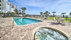 A swimming pool with a hot tub, surrounded by lounge chairs and a fenced area with palm trees. - Prime Location + Ocean View: Myrtle Beach Condo! (Myrtle Beach)