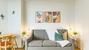 A modern living room with a grey sofa, wooden chairs, a small table, and wall-mounted artwork. - Prime Location + Ocean View: Myrtle Beach Condo! (Myrtle Beach)