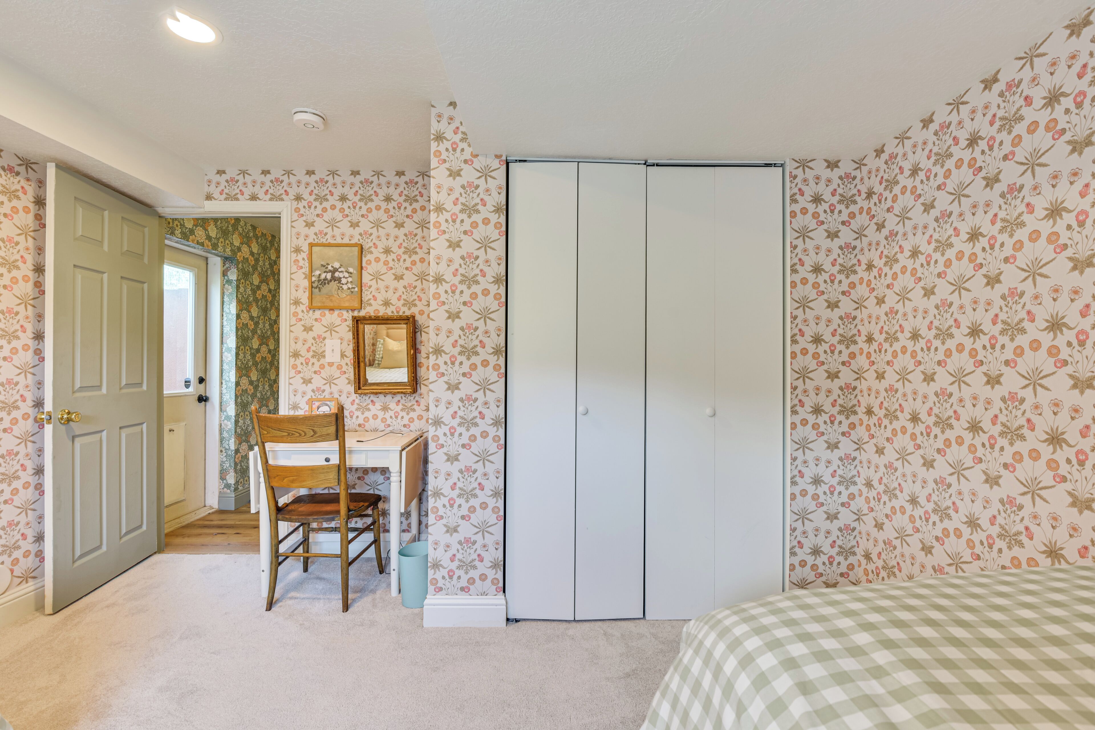 A bedroom with a bed, a desk with a chair, a wardrobe, and a door leading to another room.