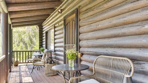 A log cabin with a wooden porch, wicker furniture, a round table, and a flower vase. - Ski, Hike & More: Homey Huntsville Retreat! (Huntsville)