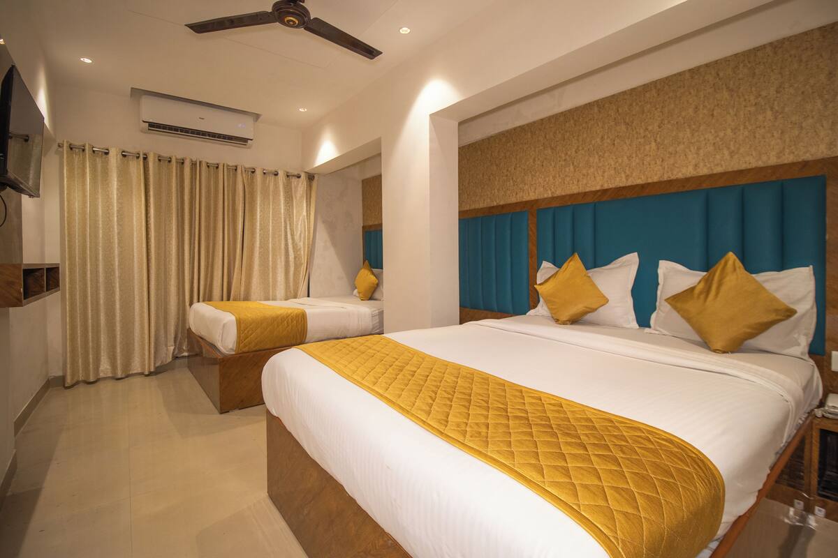 Habitación de hotel con dos camas, ventilador de techo, aire acondicionado y televisor en la pared.