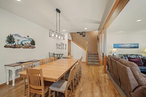 Un espace repas avec une table et des chaises en bois, un lustre et un escalier menant à une autre pièce.
