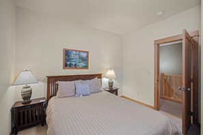 Un lit bien fait, avec une tête de lit, deux tables de chevet avec des lampes, un tableau encadré au mur et une porte en bois.