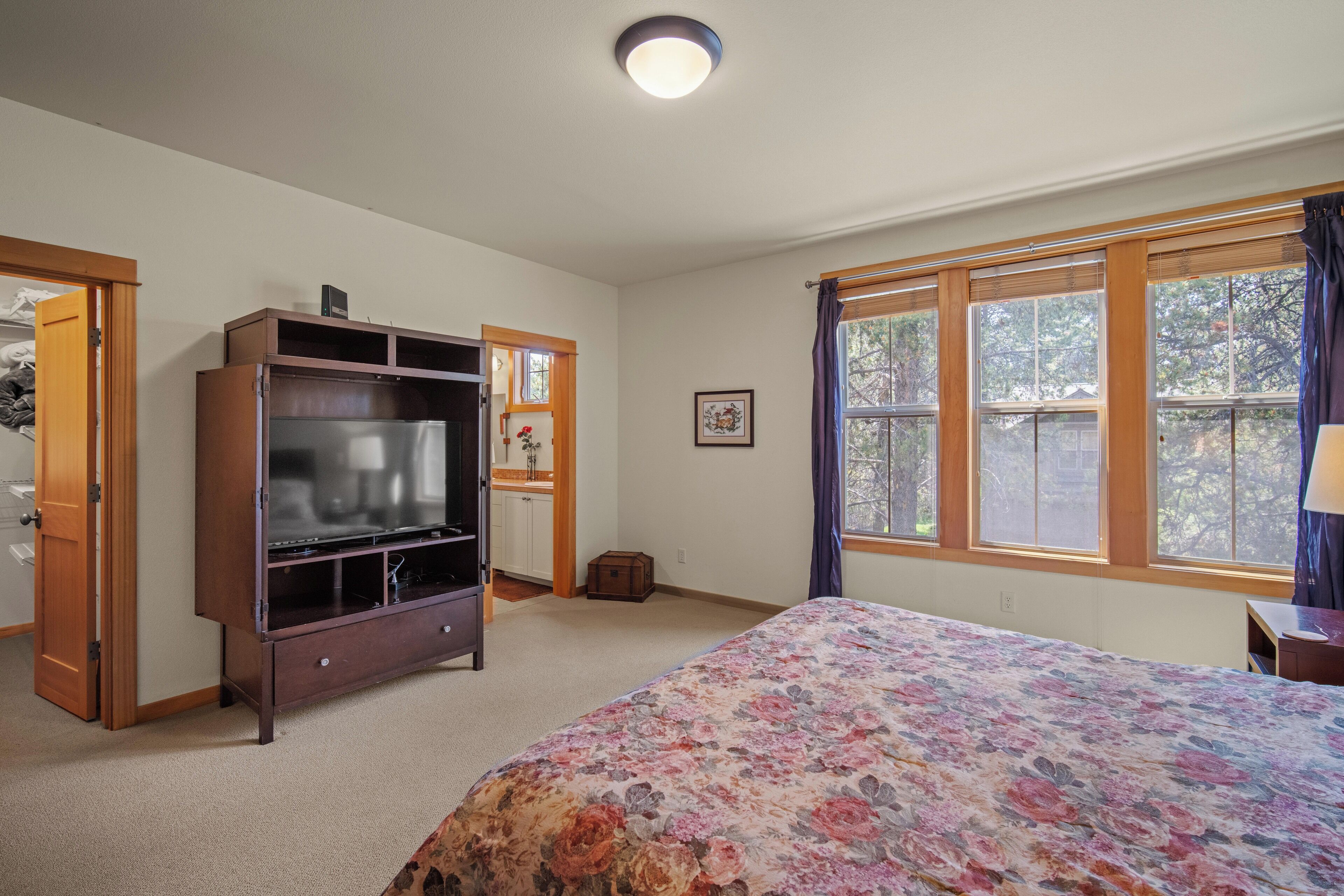 A bedroom with a bed, a wooden cabinet, a television, a window with curtains, and a door.