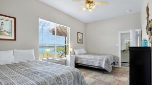 Ein Schlafzimmer mit zwei Betten, einem Deckenventilator, einem Fenster mit Jalousien und Blick ins Freie.