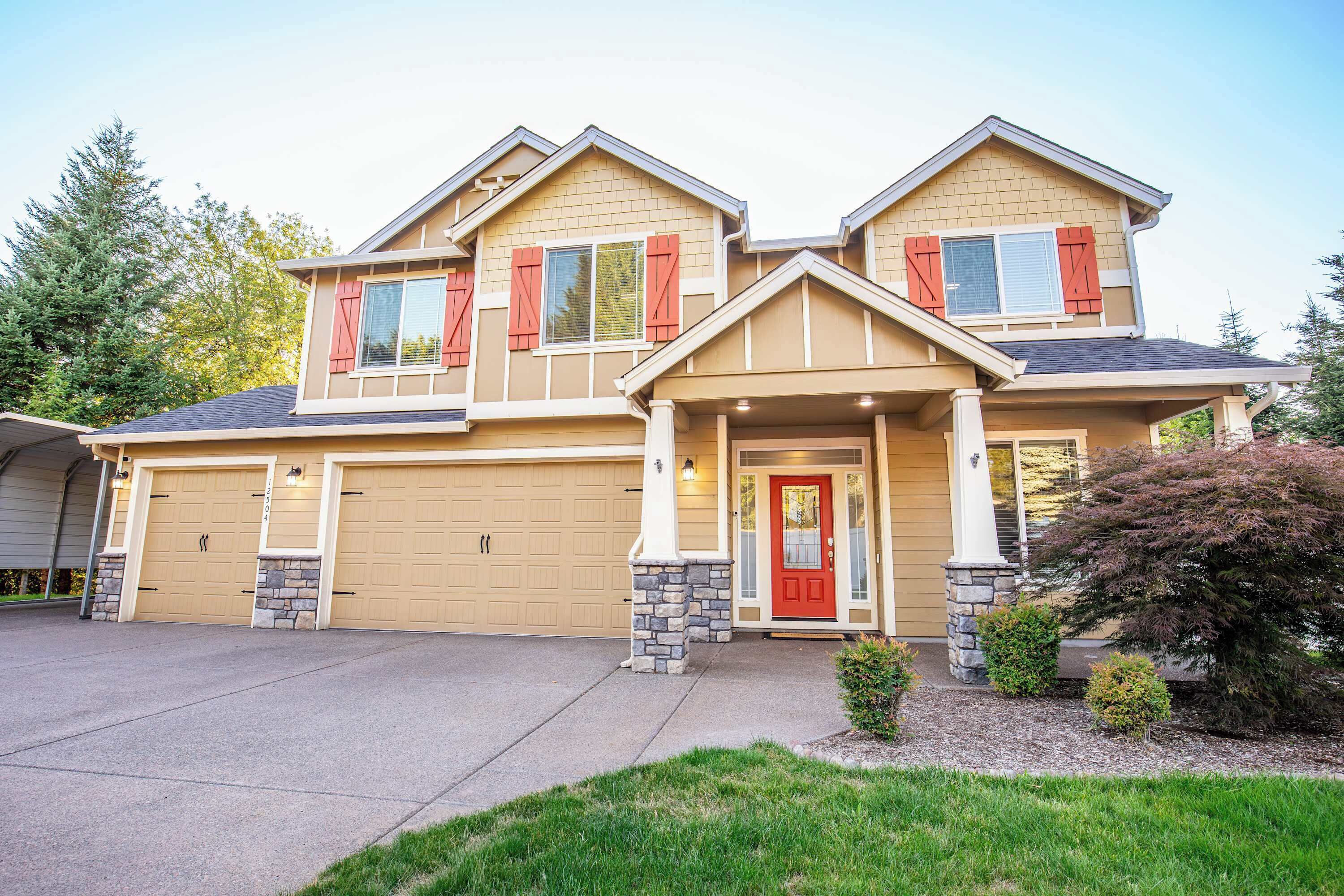 A two-story house with a beige exterior, red shutters, and a stone foundation.