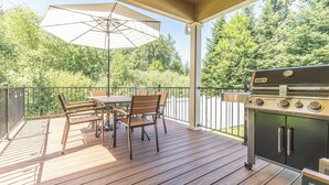 A covered outdoor patio with a wooden deck, a table with chairs, a grill, and a large umbrella.