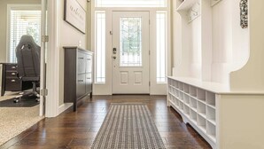 A hallway with a white door, a desk with a chair, and a shelving unit with hooks.